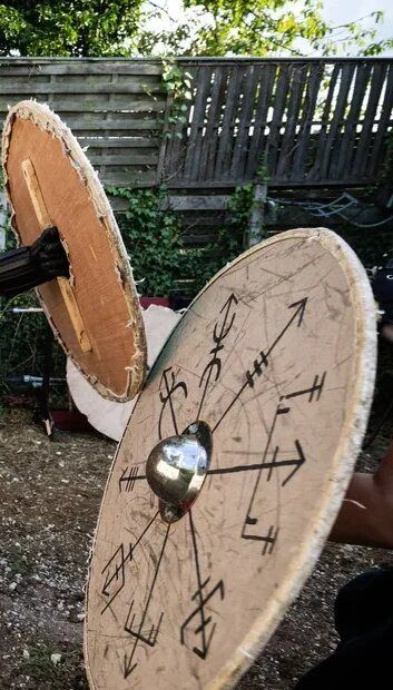 Deux boucliers ronds vikings dressés dans un jardin, l’un peint de runes.