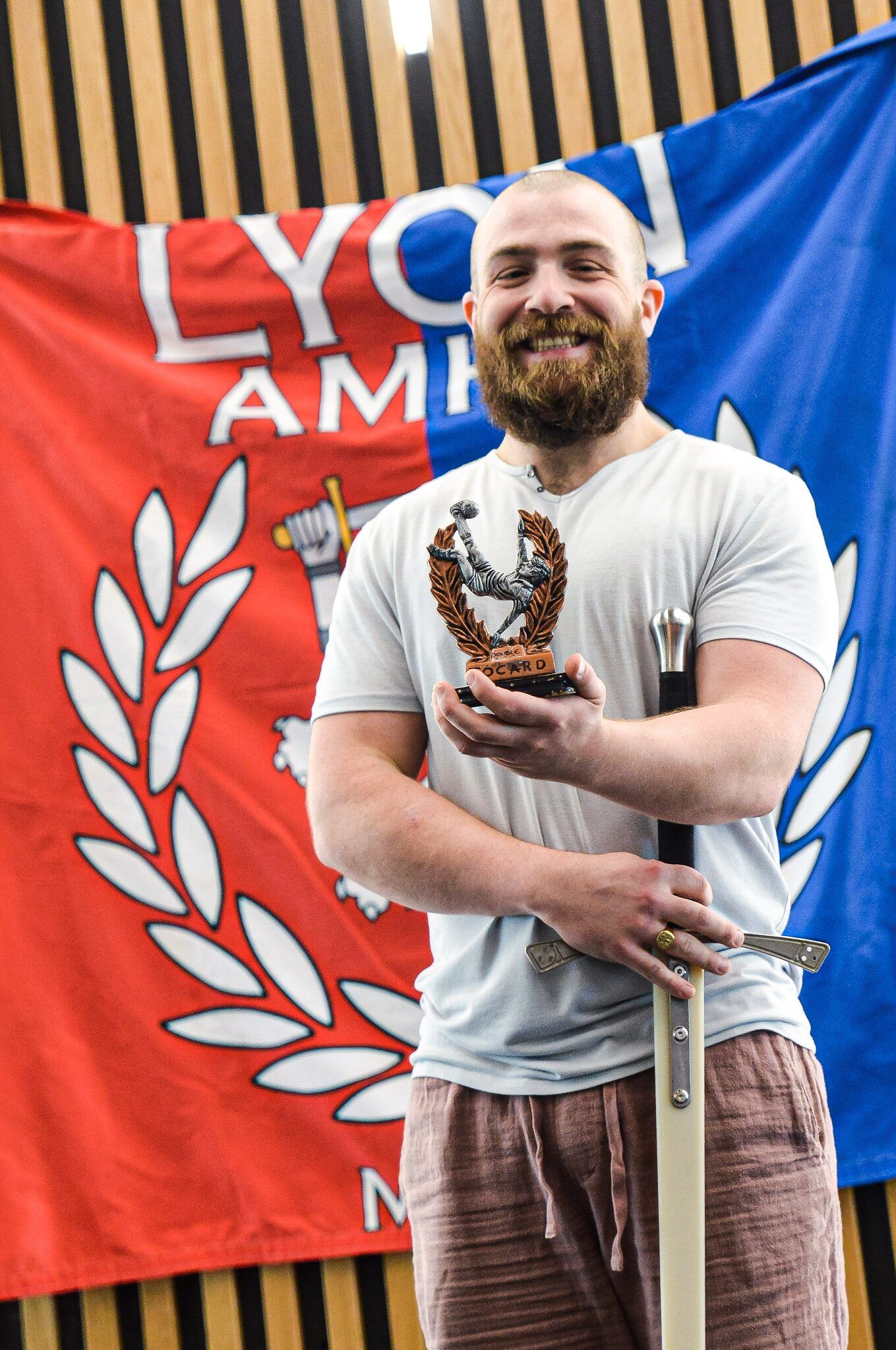 Un membre du club sourit avec son trophée, devant le drapeau du tournoi.